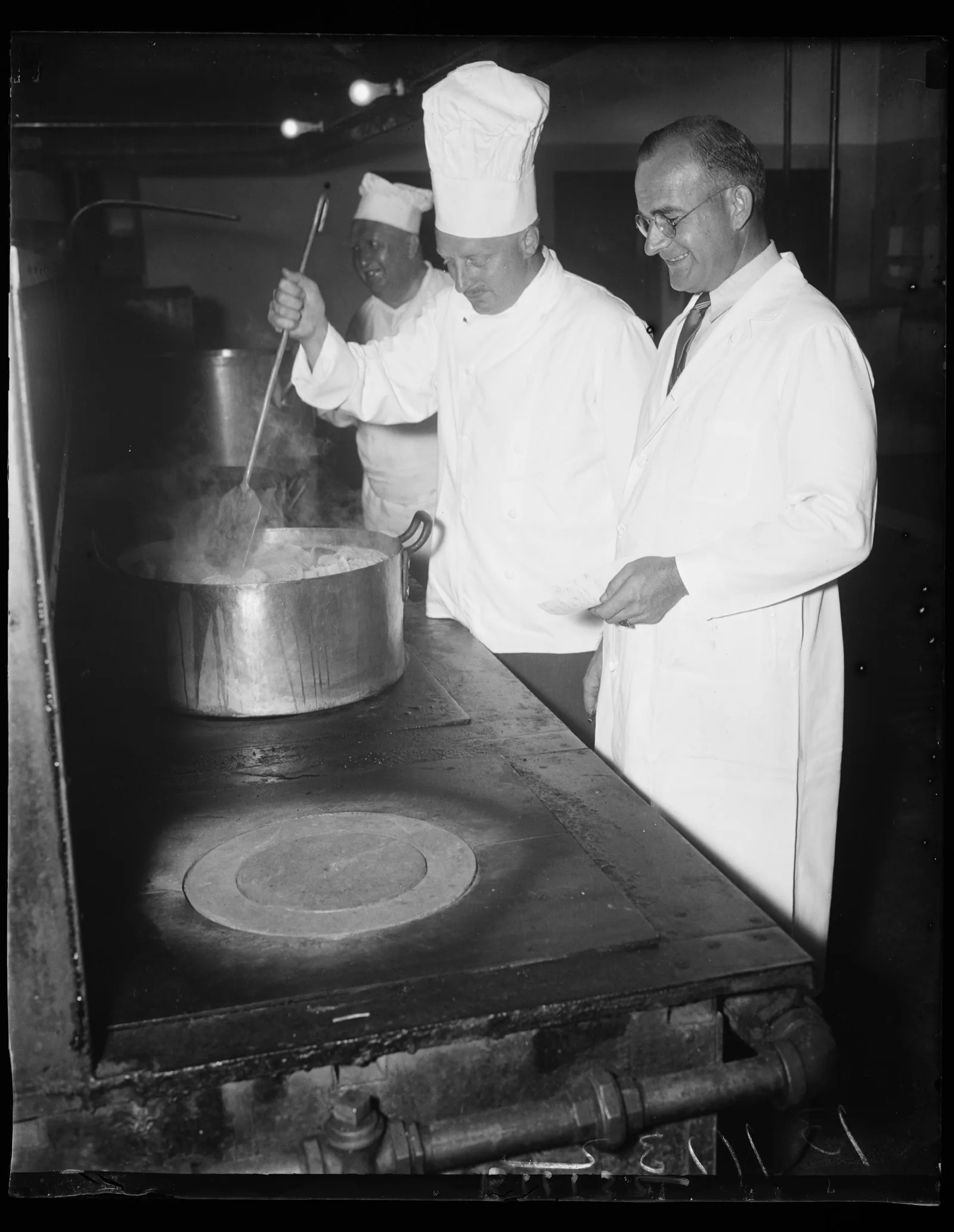 A chef in whites works over a long counter of prepared plates in a hotel kitchen, Washington, 1936