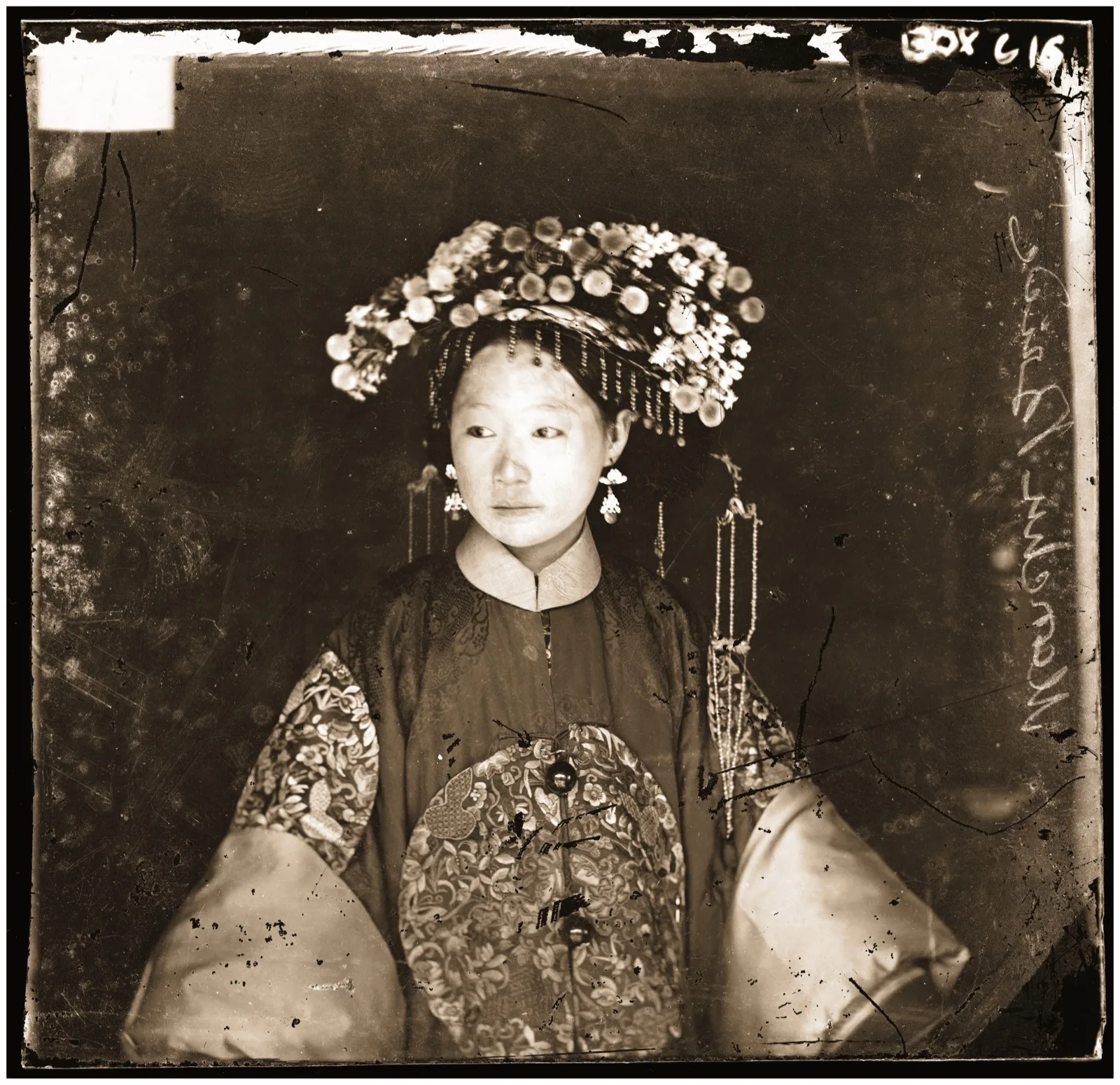 A glass-negative portrait of a young Manchu bride in an embroidered robe and a headdress hung with flowers and beads, facing the camera