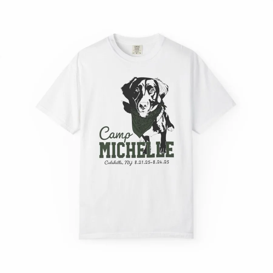 A white garment-dyed t-shirt printed with a drawing of a dog in a bandana above the words Camp Michelle, Catskills New York